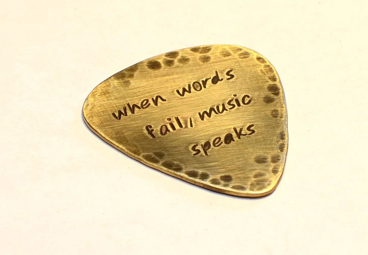 When Words Fail Music Speaks stamped on a rustic handcrafted brass guitar pick