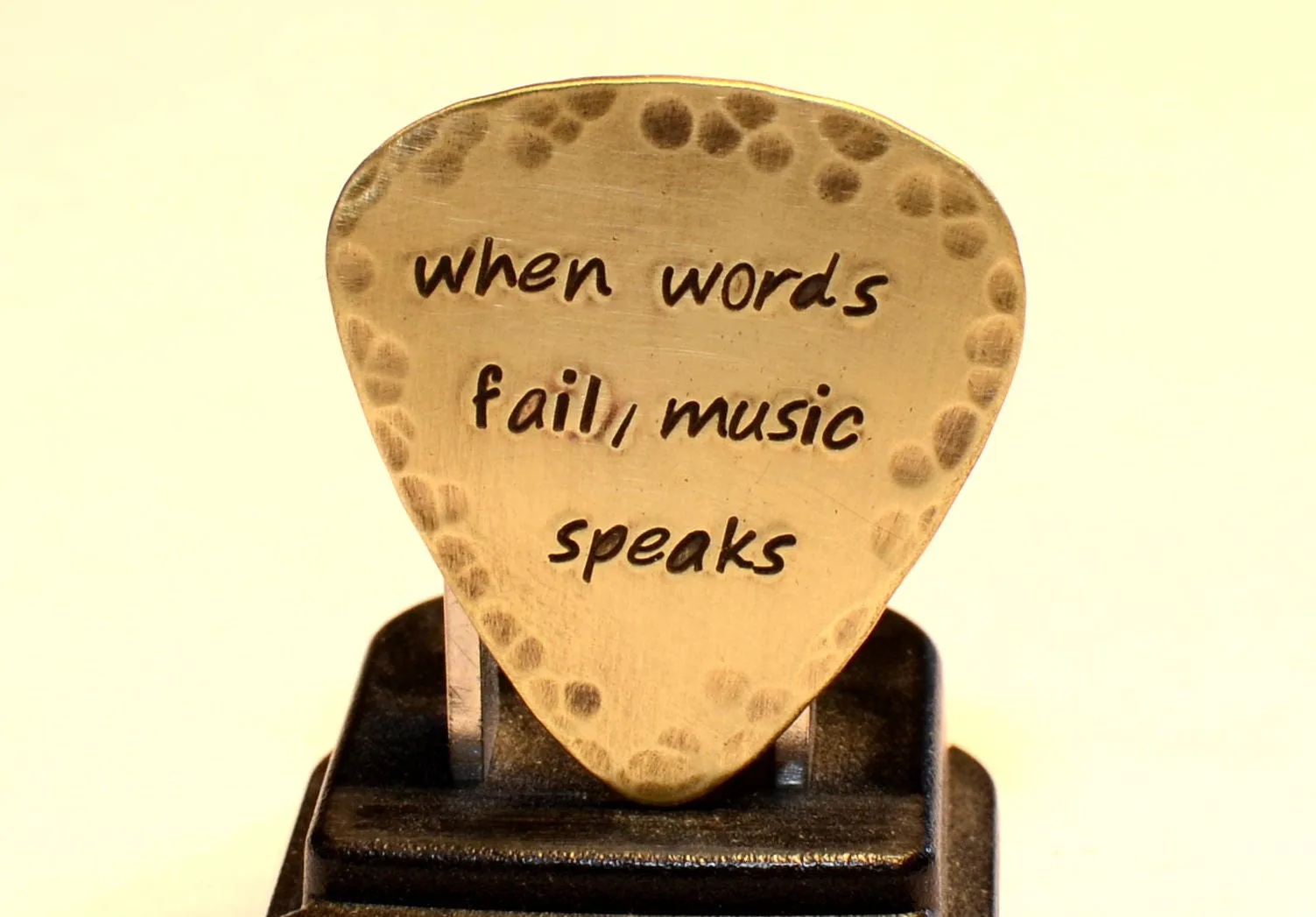 When Words Fail Music Speaks stamped on a rustic handcrafted brass guitar pick