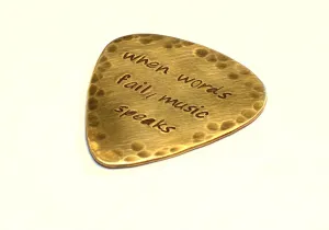When Words Fail Music Speaks stamped on a rustic handcrafted brass guitar pick