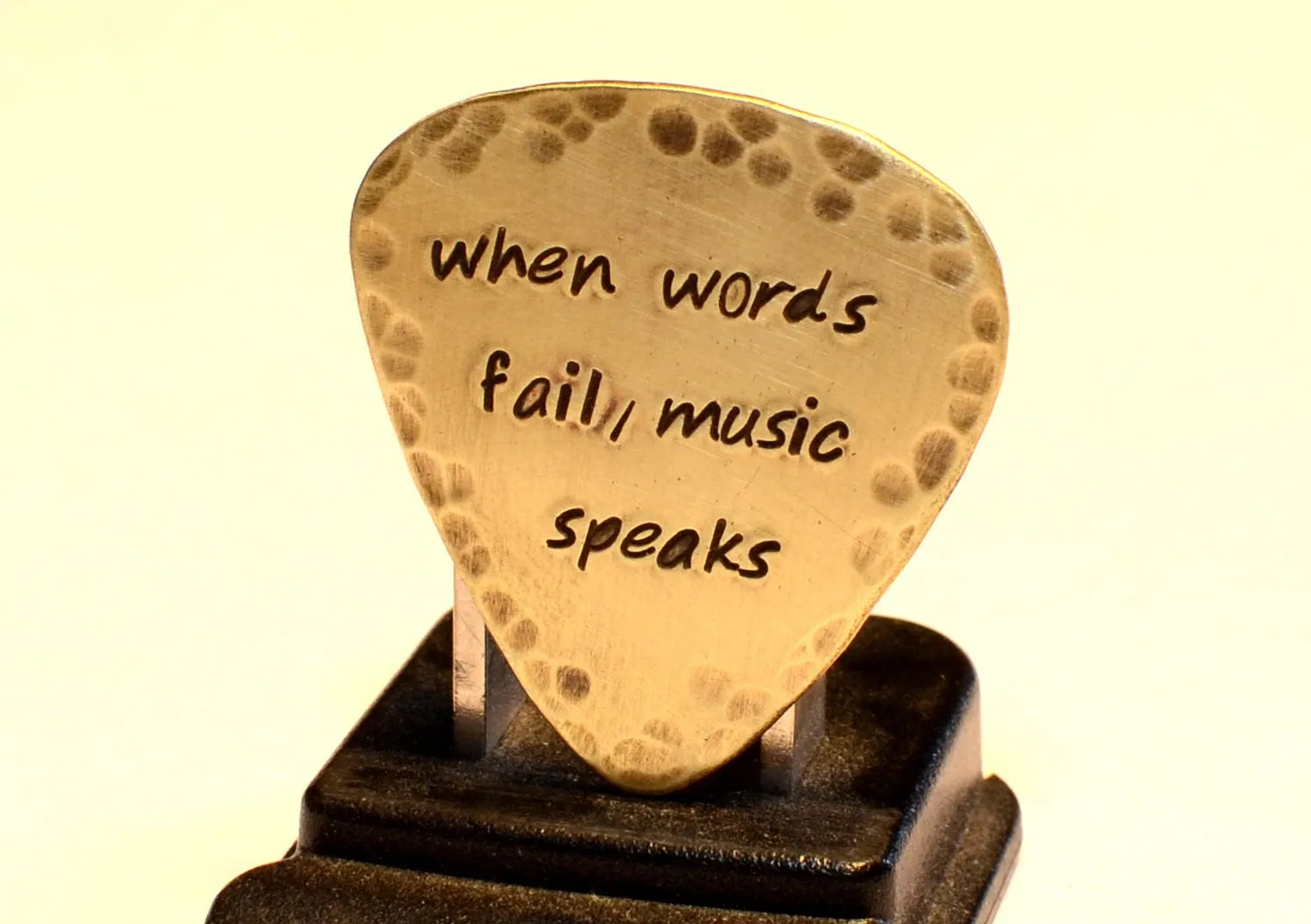 When Words Fail Music Speaks stamped on a rustic handcrafted brass guitar pick